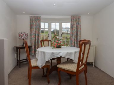 A dining room with a round table covered with a white cloth and four chairs floral curtains and a window at Badger's Den in Budleigh Salterton