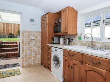 A kitchen with wooden cabinets a washing machine a sink and door leading to a garden at Badger's Den in Budleigh Salterton