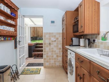 A kitchen with wooden cabinets a washing machine a microwave and a door leading outside at Badger's Den in Budleigh Salterton