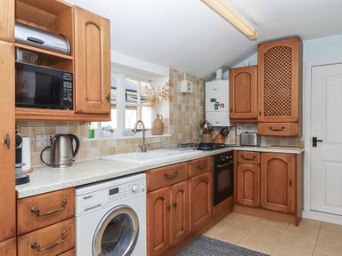 A kitchen with wooden cabinets a washing machine a microwave kettle toaster and a sink at Badger's Den in Budleigh Salterton