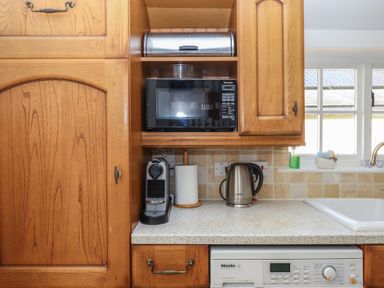 A kitchen counter with a coffee machine paper towel roll electric kettle microwave and bread box at Badger's Den in Budleigh Salterton