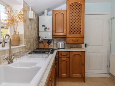 A kitchen with wooden cabinets a white sink and a gas stove at Badger's Den in Budleigh Salterton