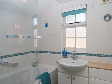 A bathroom with a bathtub a sink a window and a blue towel at Badger's Den in Budleigh Salterton