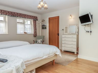 A bedroom with two beds a wooden door a white chest of drawers and a wall-mounted tv at Badger's Den in Budleigh Salterton