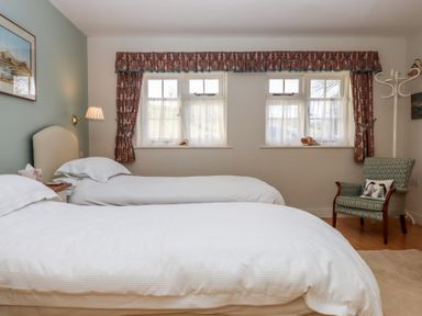 A bedroom with two single beds a green armchair and windows with curtains at Badger's Den in Budleigh Salterton