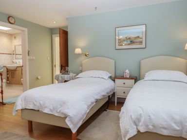 A bedroom with two single beds bedside tables a small round table and an open door leading to a bathroom at Badger's Den in Budleigh Salterton