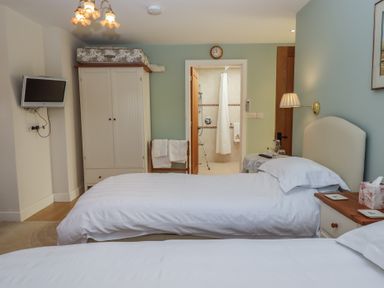 A bedroom with two single beds a wardrobe a wall-mounted TV and an open door leading to a bathroom at Badger's Den in Budleigh Salterton