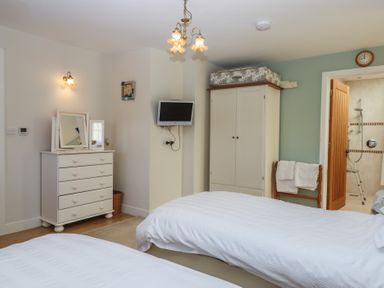 A bedroom with two beds a white dresser and a wardrobe with a bathroom visible through an open door at Badgers Den in Budleigh Salterton