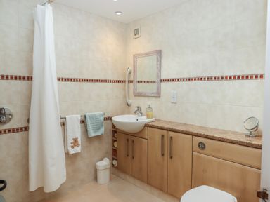A bathroom with a shower curtain towel rack sink mirror and wooden cabinets at Badgers Den in Budleigh Salterton