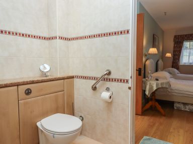 A bathroom with a toilet and countertop next to a bedroom with two beds and a bedside table at Badger's Den in Budleigh Salterton