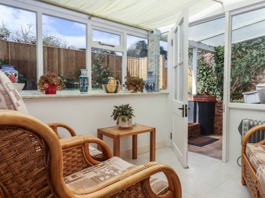 A sunroom with wicker chairs a small wooden table and pottery on the window ledge at Badger's Den in Budleigh Salterton