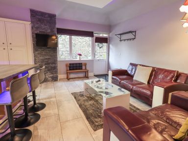 A living room with leather sofas a glass coffee table bar stools and a wall mounted television at 1 The Old Coach House in Ambleside