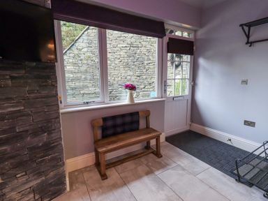 An entryway with a wooden bench and a wall-mounted television at 1 The Old Coach House in Ambleside