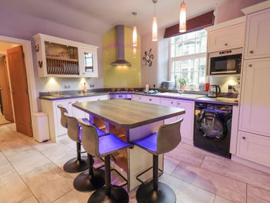 A kitchen with an island and four bar stools a washing machine and microwave above the counter at 1 The Old Coach House in Ambleside