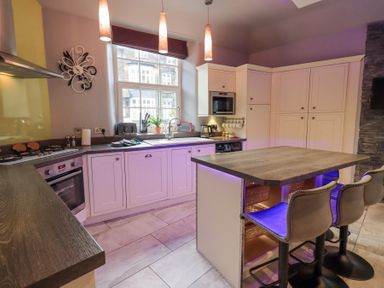 A kitchen with a breakfast bar three stools pendant lights and cabinets at 1 The Old Coach House in Ambleside