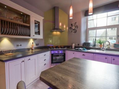 A kitchen with white cabinets a stove a sink and large windows at 1 The Old Coach House in Ambleside