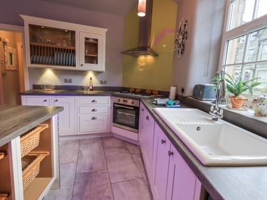 A kitchen with white cabinets a sink a stove and a window with plants at 1 The Old Coach House in Ambleside