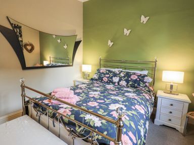 A bedroom with a metal bed frame floral bedding two bedside tables with lamps and butterflies on a green accent wall at 1 The Old Coach House in Ambleside