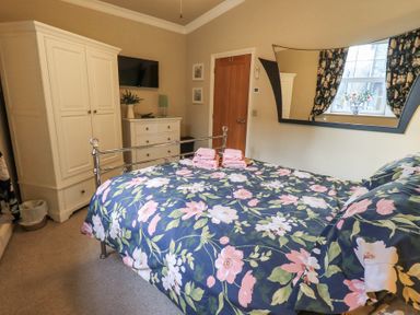 A bedroom with a floral bedspread two white wardrobes a chest of drawers and a window at 1 The Old Coach House Ambleside