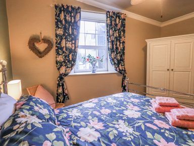 A bedroom with a metal bed frame floral bedding and matching curtains a white wardrobe and a window with flowers at 1 The Old Coach House in Ambleside