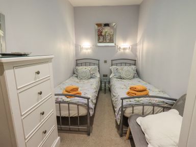 A bedroom with two single metal beds with floral bedding and orange towels a white dresser and a chair with pillows at 1 The Old Coach House in Ambleside