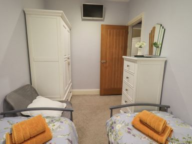 A bedroom with two beds and orange towels on them a chair wardrobe and chest of drawers at 1 The Old Coach House in Ambleside
