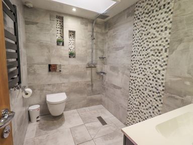 A bathroom with a wall-mounted toilet and a walk-in shower with decorative tiles and a sink at 1 The Old Coach House in Ambleside
