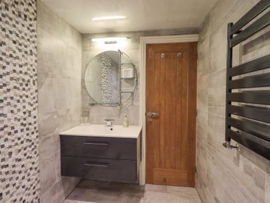 A bathroom with a floating sink vanity round mirror wooden door and heated towel rail at 1 The Old Coach House in Ambleside