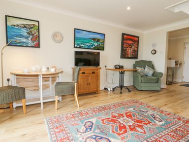 A living room with patterned rug chairs small tables armchair and paintings on walls at Carningli Suite near Newport
