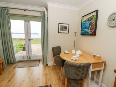 A dining area with a wooden drop-leaf table and two chairs near glass doors with green curtains showing an outdoor view at carningli suite near newport
