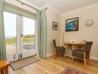 A small dining area with a wooden table set with tea service two chairs a floor lamp and paintings on the wall next to glass doors with curtains at Carningli Suite near Newport