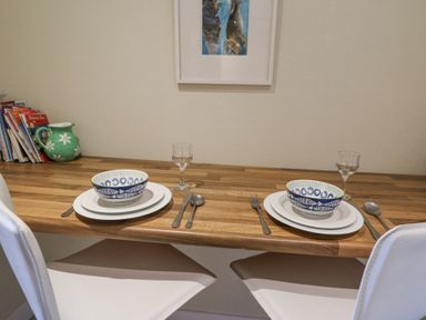 A wooden dining table set for two with bowls plates cutlery and glasses with books and a green jug on the side at Carningli Suite near Newport