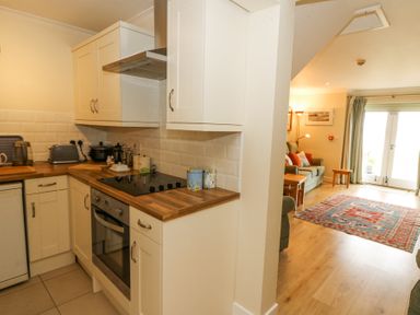 A kitchen with white cabinets wooden countertops and an electric stove next to a living room with sofas a colorful rug and double doors at Carningli Suite near Newport