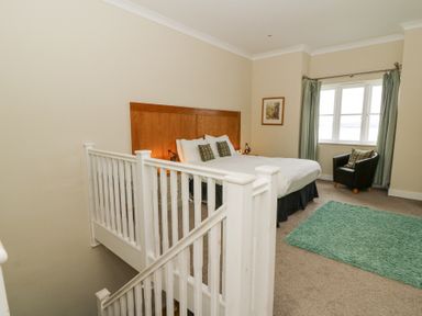 A bedroom with a bed an armchair a green rug and stairs with a white railing at Carningli Suite near Newport