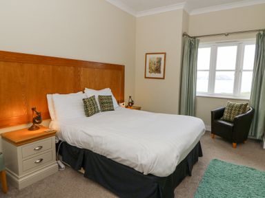 A bedroom with a double bed nightstands a chair and a window with curtains at Carningli Suite near Newport