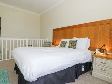 A bedroom with a large bed white bedding wooden headboard side tables and lamps at Carningli Suite near Newport