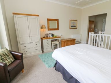 A bedroom with a bed a desk with a lamp a wardrobe an armchair and a mirror at Carningli Suite near Newport