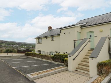 An exterior view of a building with stairs leading to green doors and parking spaces near a countryside at Carningli Suite near Newport