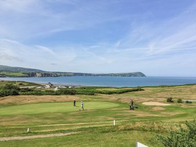 A golf course with people playing near a coastline with cliffs and a beach at Carningli Suite near Newport