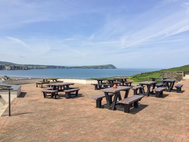 An outdoor patio with picnic tables overlooking the ocean and cliffs at Carningli Suite near Newport