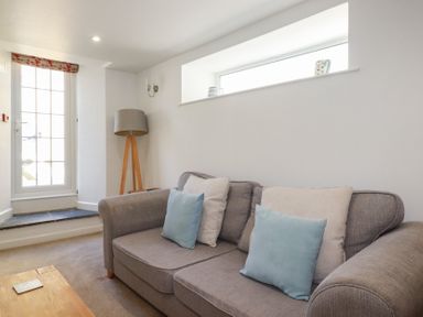 A living room with a grey sofa and cushions next to a window and a floor lamp at St Georges in Padstow
