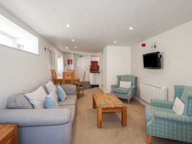 A living room with a grey sofa and blue armchairs with pillows a wooden coffee table and dining table with chairs at St Georges in Padstow