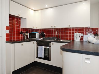 A kitchen with white cabinets red tiled backsplash and black countertops at St Georges in Padstow