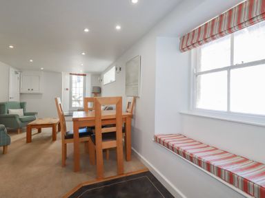 A room with a wooden dining table and chairs two armchairs and a window with a striped cushion at St Georges in Padstow