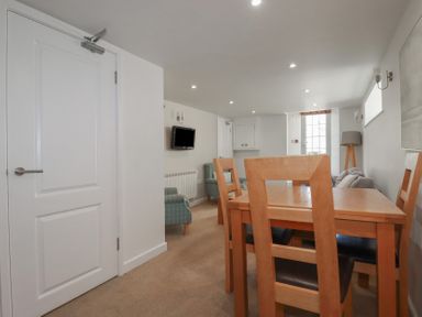 A dining area with a wooden table and chairs and a TV mounted on the wall in a room at St Georges in Padstow