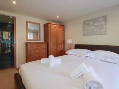 A bedroom with a double bed white linens rolled towels wooden wardrobe chest of drawers mirror and bedside lamp at St Georges in Padstow