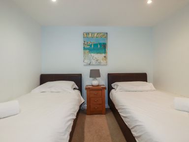 A bedroom with two single beds a wooden nightstand with a lamp and a painting on the wall at St Georges in Padstow