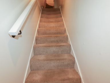 A carpeted staircase with white walls and a white handrail on one side at St Georges in Padstow