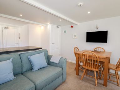 A living room with a blue sofa and wooden dining table with four chairs and a wall-mounted TV at St Saviours Padstow