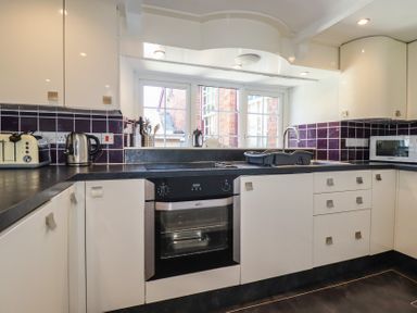 A kitchen with white cabinets black countertops a built in oven a kettle a toaster and a microwave at St Saviours in Padstow